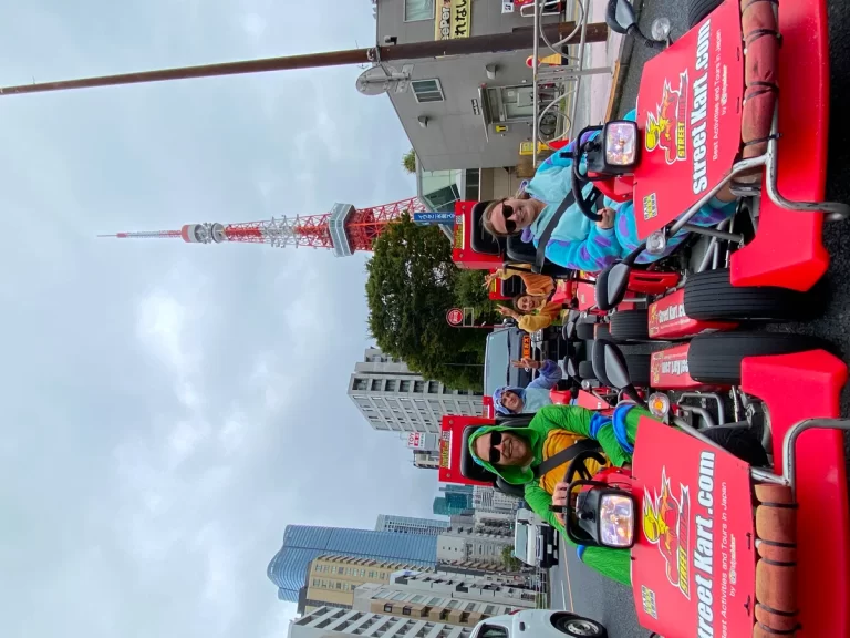 People riding red go-karts in a city street parade, with tall buildings and a red-and-white tower in the background and signs on the karts reading speedkart.com.